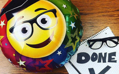 A smiley graduation balloon on a table next to some glasses and paper saying done